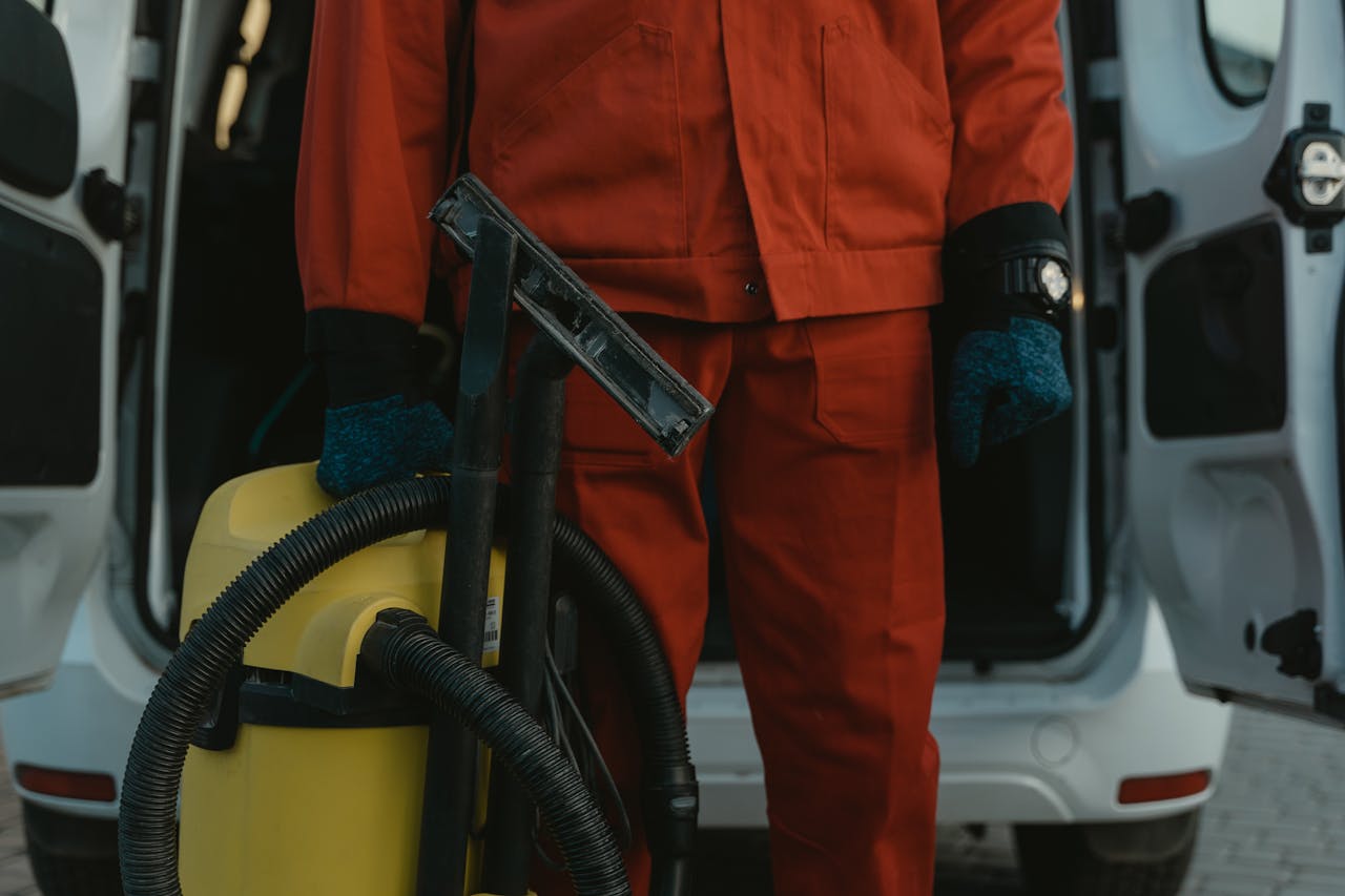hero-img A professional cleaner in a red uniform holding a vacuum near a van, ready for service.