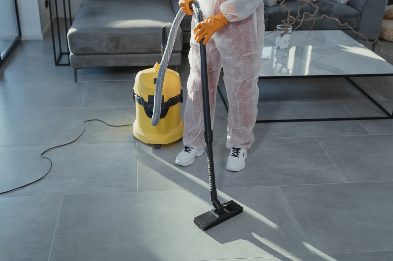 about-01 A professional cleaner in protective gear vacuuming the floor in a modern living room.
