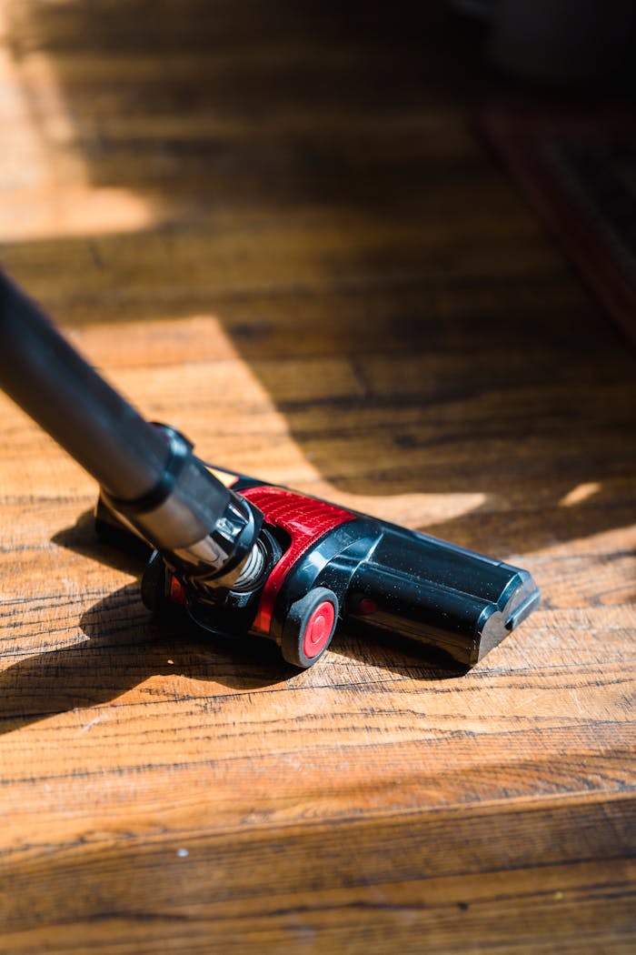 services-01 A high-angle view of a vacuum cleaner head working on a sunlit wooden floor.